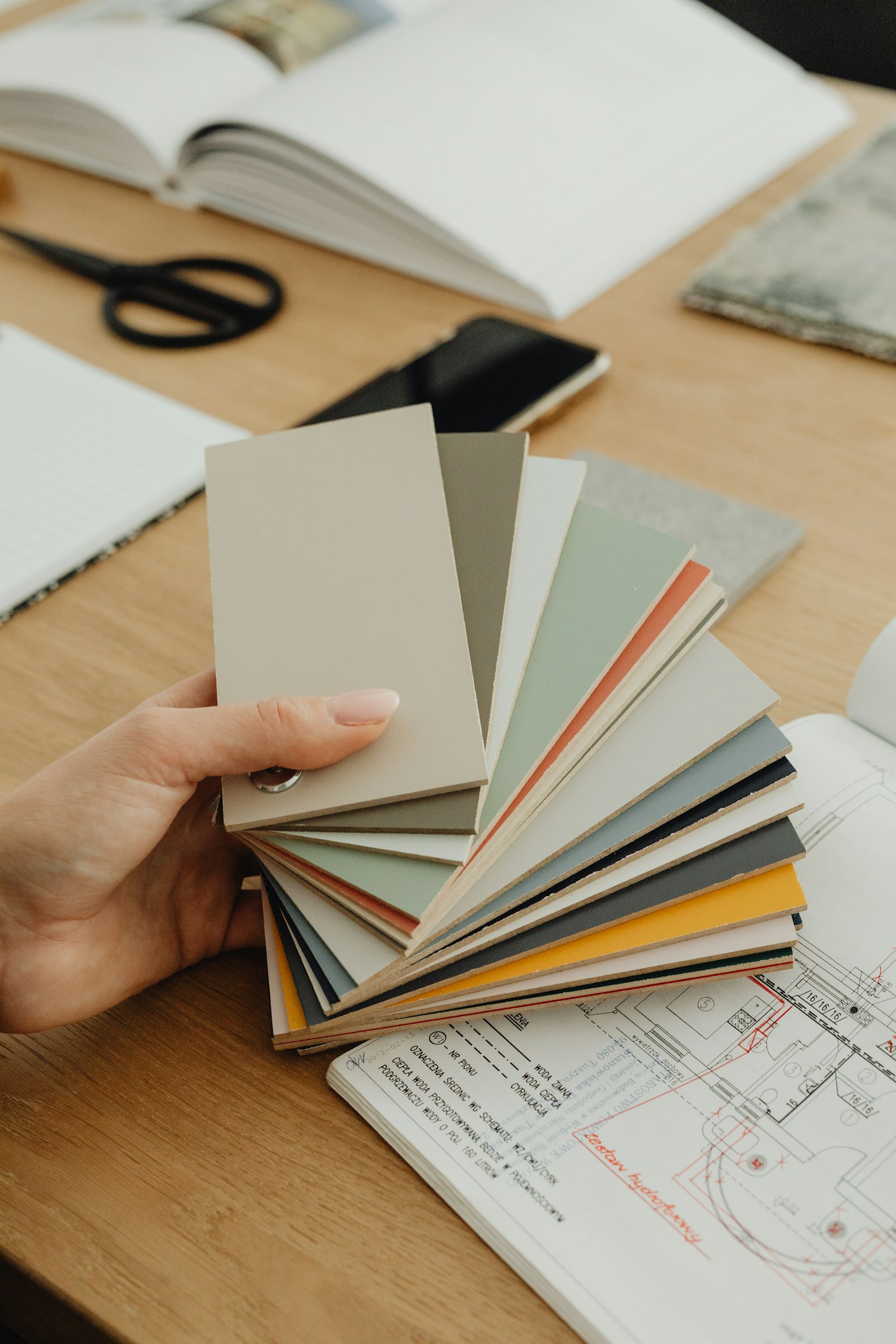 Hand fanning out paint and material color swatches over a floor plan during a design consultation